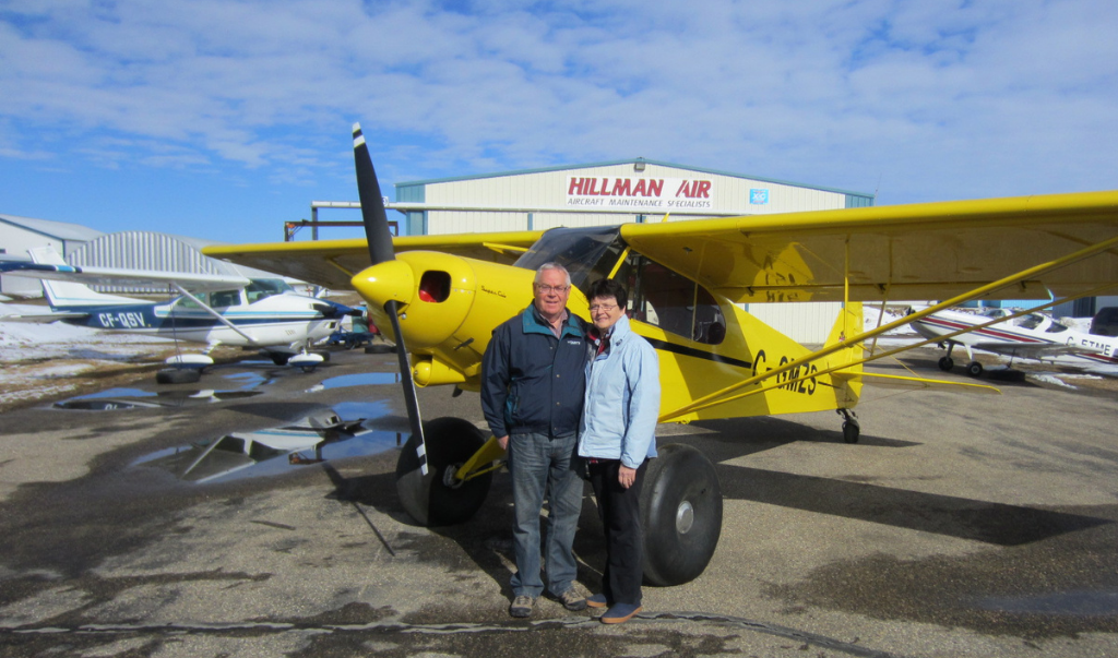Mr. and Mrs. Hillman posing in front of small aircraft outside their hangar at Hillman Air (AV)